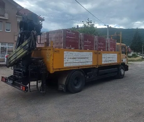 Žuti CAJA kamion s dizalicom natovaren građevinskim materijalom